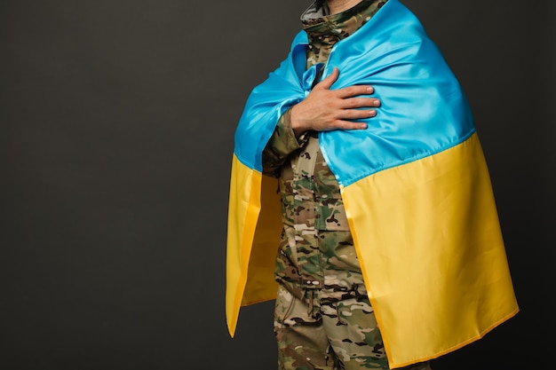 Photo portrait of a courageous ukrainian military man tied with the flag of ukraine and holding hand on heart freedom concept