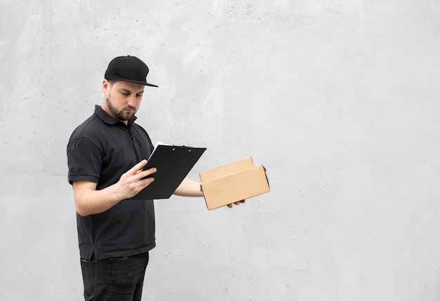 Photo portrait of courier with order papers and packages with food near grey wall