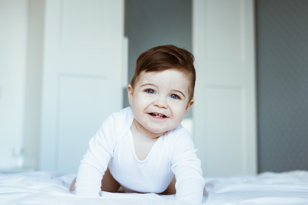 Portrait of a crawling and smilling boy baby on the bed in bedroom. Happy childhood concept side view