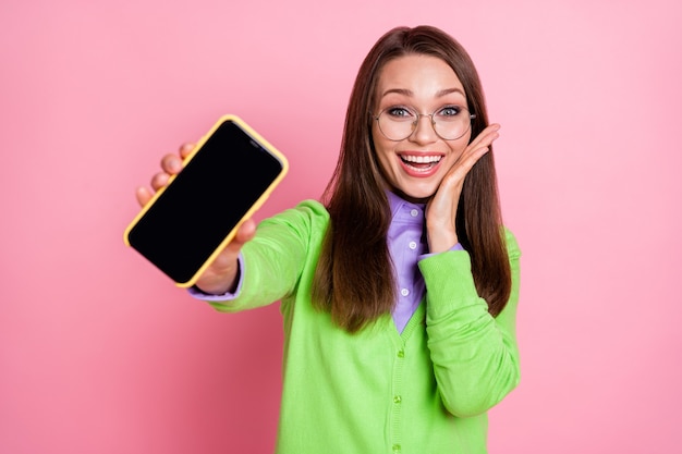 Il ritratto della ragazza stupita pazza tiene lo smartphone isolato sopra il fondo di colore pastello