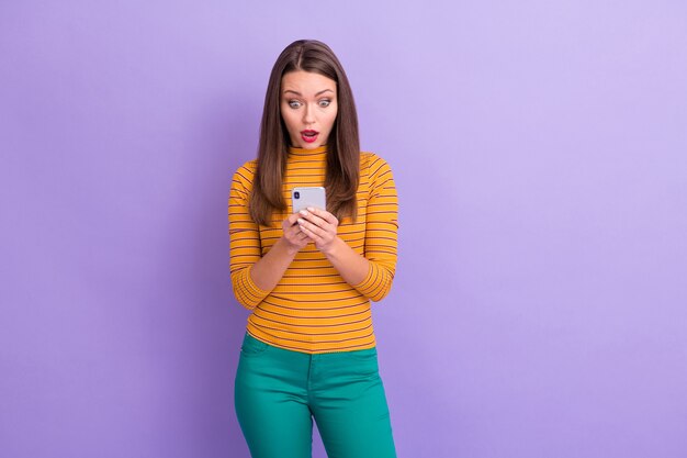 Portrait of crazy astonished girl social network user use smart phone read comment feedback impressed scream wow omg wear good look jumper trousers isolated over purple color