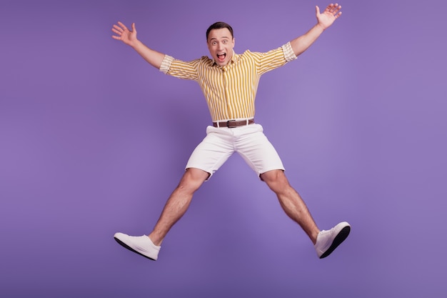 Portrait of crazy astonished guy jump star pose dance on purple background