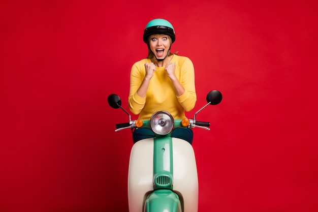 Portrait of crazy overjoyed girl sitting on moped raise fists