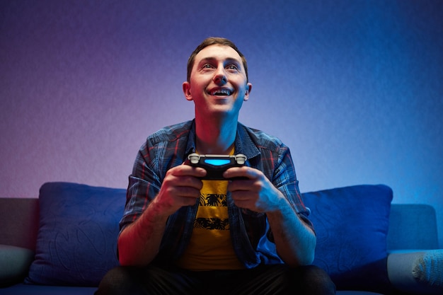 Portrait of crazy playful Gamer, boy enjoying Playing Video Games indoors sitting on the sofa, holding Console Gamepad in hands. Resting At Home, have a great Weekend