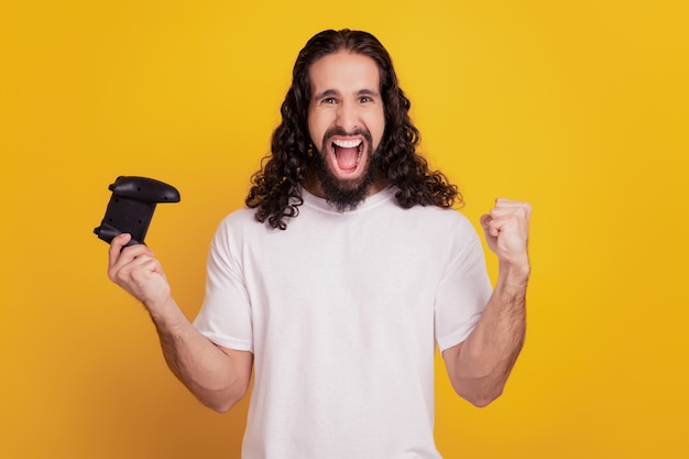 Portrait of crazy positive guy hold joystick win videogame scream on yellow background