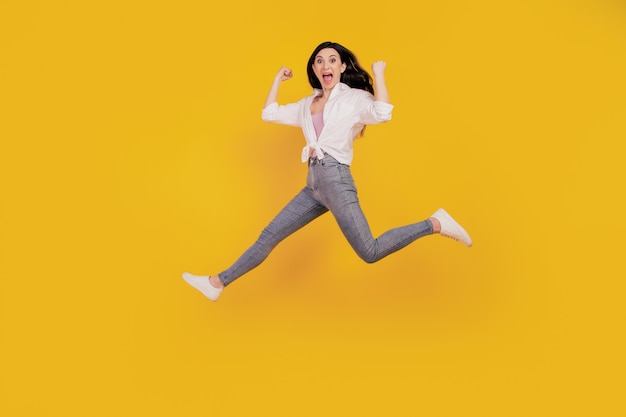 Portrait of crazy sporty active girl raise fists open mouth jump run on yellow background