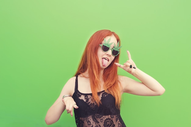 Portrait of a crazy stylish girl showing rock gesture on green 