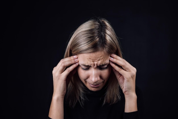 Ritratto di donna che piange con le dita della mano a faccia in giù che toccano le tempie su sfondo nero vittima di abusi fisici e psicologici gaslighting aggressione relativa