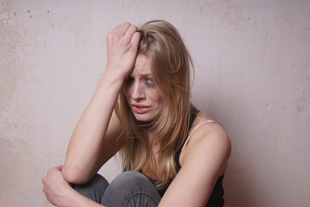 Photo portrait of crying young woman sitting against wall