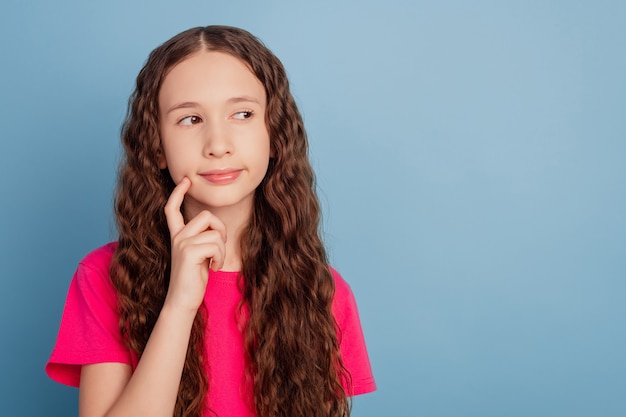 Portrait of cunning smart clever little girl finger cheek look copyspace on blue background