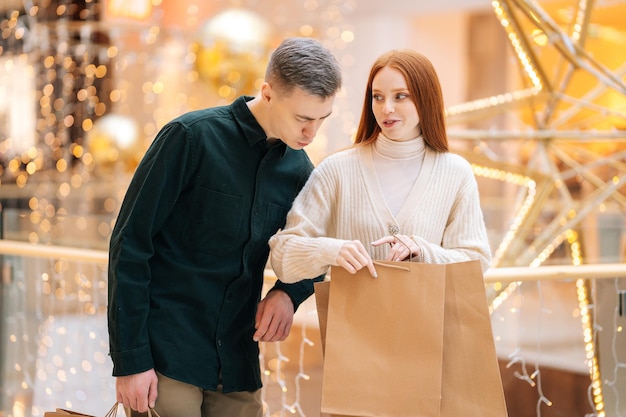 Portrait of curiosity young couple walking shopping mall holding shopping bags looking inside