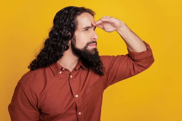 Portrait of curious explorer guy hand forehead look blank space on yellow background