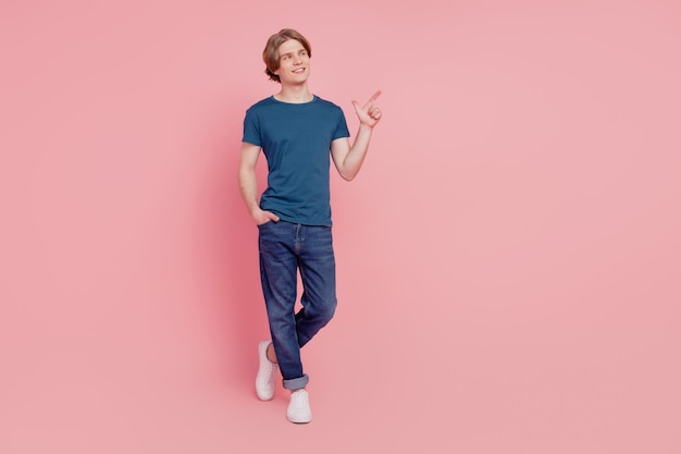 Portrait of curious positive promoter guy indicate finger empty blank space look up on pink background