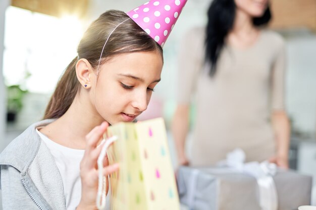 Portrait of curious teenaged latin girl checking gift bag, while receiving presents, celebrating birthday with parents at home. Celebration, childhood concept