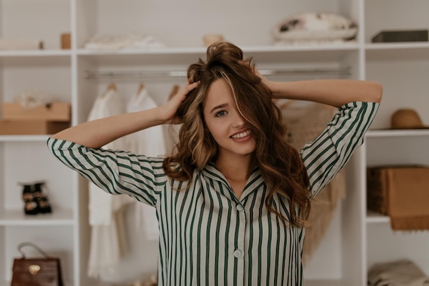 Portrait of curly charming girl ruffles hair in dressing room\
cool young woman in silk striped shi