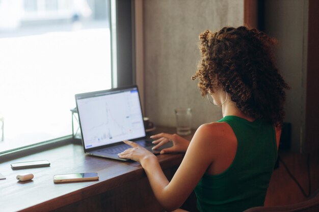 Photo portrait of curly girl using laptop sitting in cafe rear view trading cryptocurrency