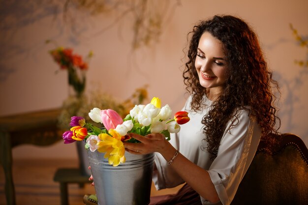 Portrait of a curly girl with a bucket of tulips. Fresh flowers for beautiful photos. Delicate photos with flowers in the studio
