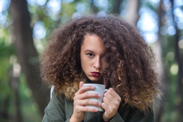 Portrait of curly hair teen girl holding mug in the park