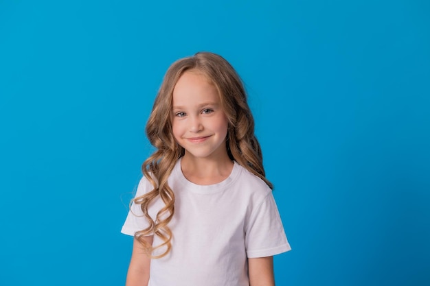 portrait of a curly-haired girl in jeans and a white T-shirt on a blue background