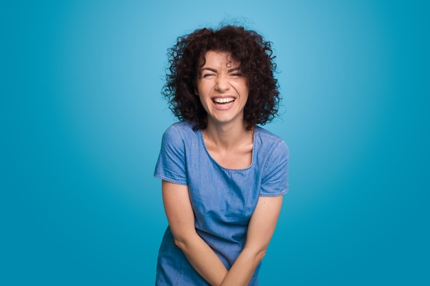 Portrait of a curly haired laughing woman posing against blue background