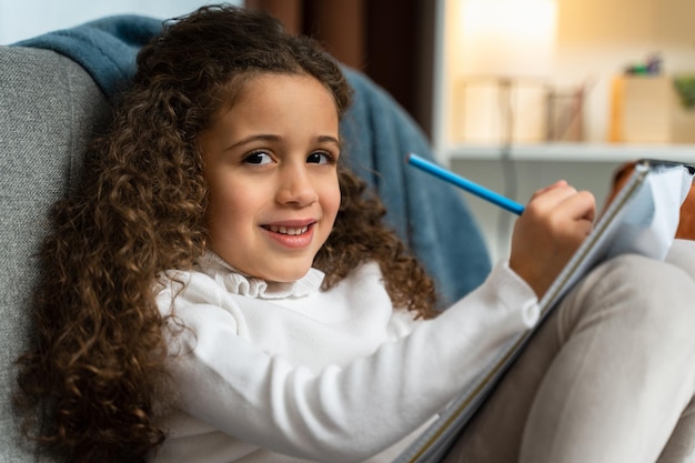 Portrait of the curly multiracial girl holding notebook while studying and doing homework at home Childhood concept