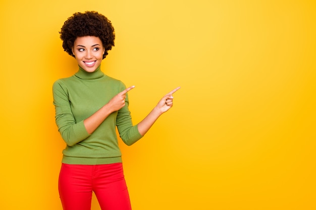 portrait of curly wavy cheerful positive woman with forefingers pointed to the empty space in red trousers showing account to follow .