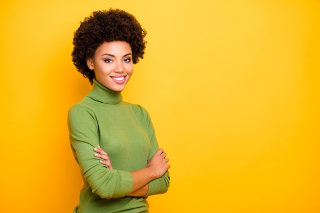 portrait of curly wavy trendy cheerful positive turned woman with arms crossed looking at you with toothy smile.