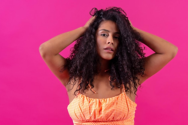 Ritratto di una donna dai capelli ricci in abiti estivi su uno sfondo rosa girato in studio