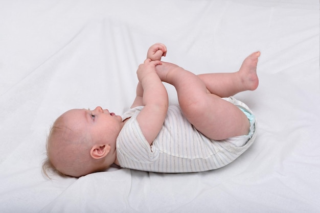 Portrait of a cute 3 months baby lying on bed Newborn lies on his back and played foot