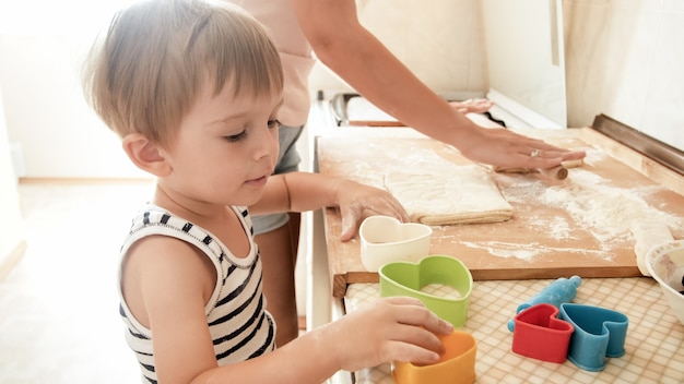 Portrait of cute 3 years old toddler boy cooking cookies with mother