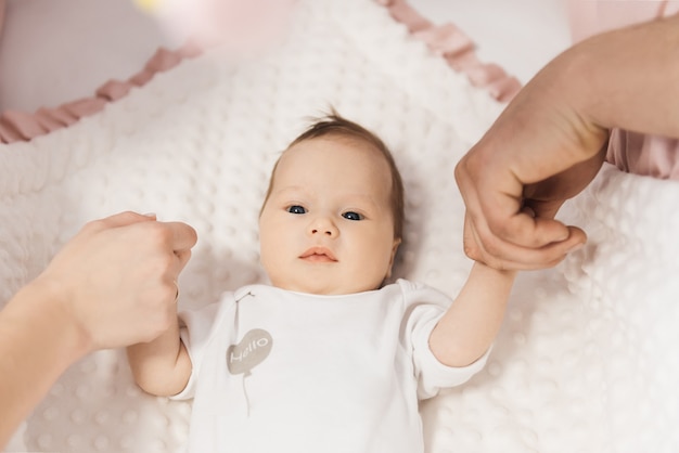 Portrait of a cute 6-month-old baby, a newborn girl lying in a crib and holding her parents ' hands