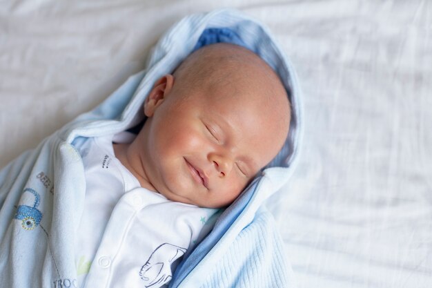 Portrait of a cute adorable baby boy sleeping on a bed on white sheet smiling in dreaming