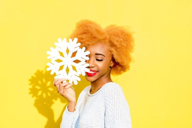 Portrait of a cute african woman in blue sweater holding an artificial snowflake on the yellow background