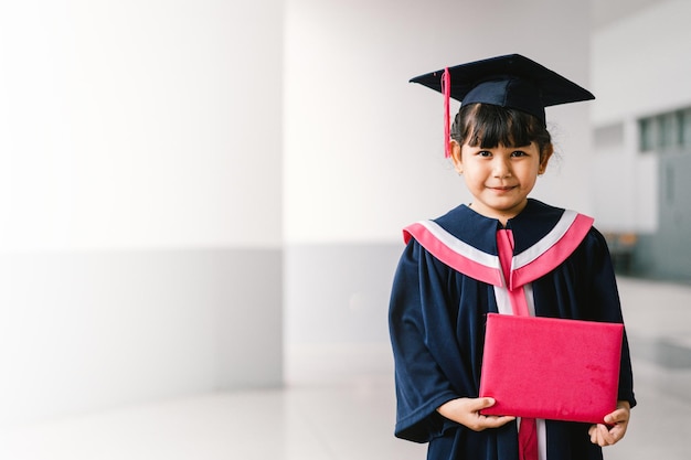 Portrait of a cute asian graduated schoolgirl with graduation\
gown in school