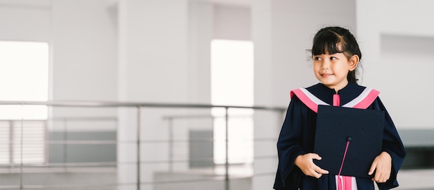 Portrait of a cute asian graduated schoolgirl with graduation\
gown in school