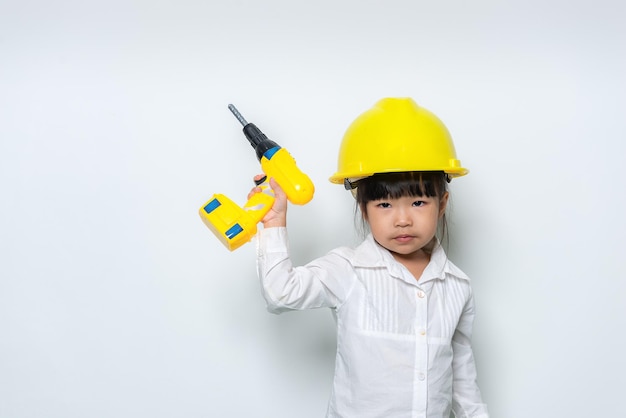 Portrait of cute asian little girl in engineer uniform and\
helmet on white background