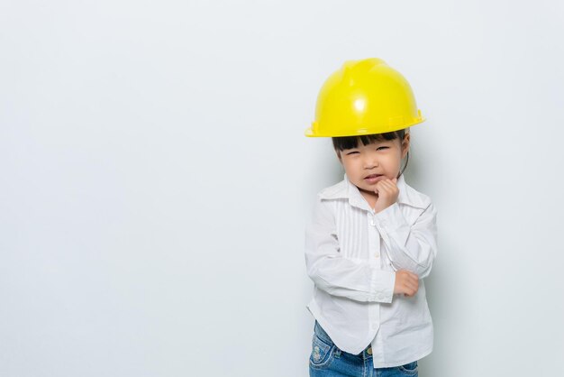 Portrait of cute asian little girl in engineer uniform and\
helmet on white background