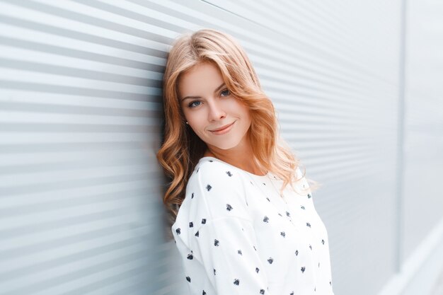 Portrait of a cute attractive young woman with a beautiful smile with blue eyes in stylish spring clothes near a metal wall outdoors in the city