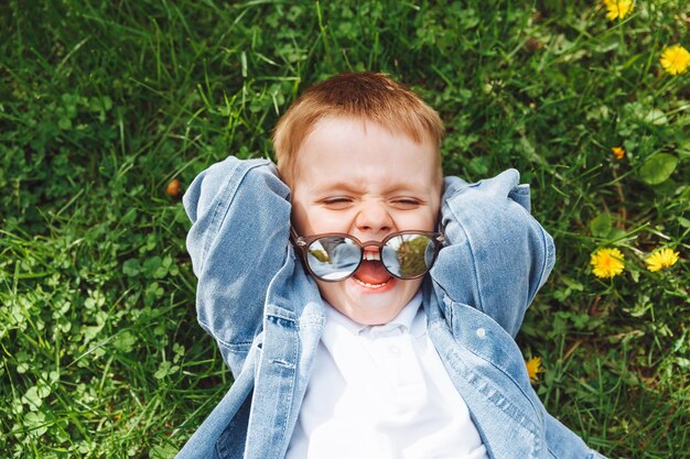 Portrait of a cute baby 4 years old Smiling lying on the grass hands under his head View from above Caucasian Spring