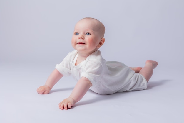 Portrait of a cute baby 5 months old in a white bodysuit on a white background in the studio smiling looking into the frame Baby39s health newborn baby space for text