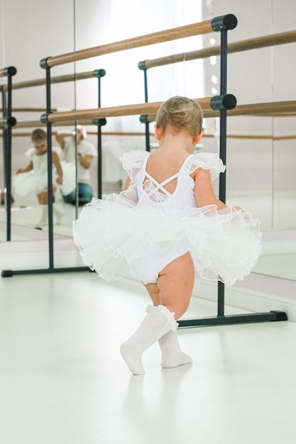 Foto ritratto di una carina ballerina che si siede vicino alla barra del ballet indossando le scarpe