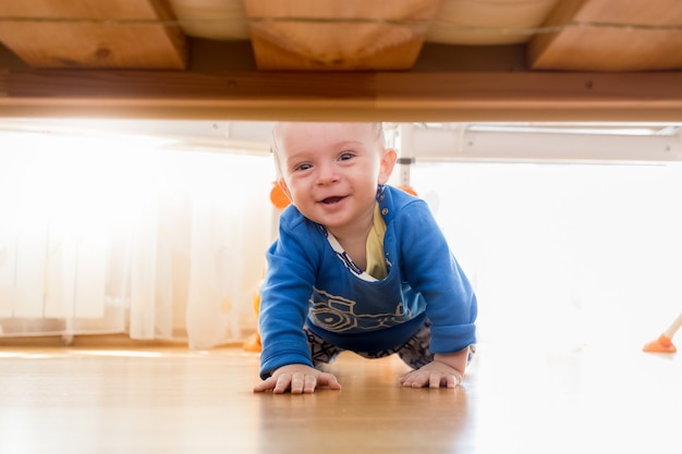 Photo portrait of cute baby boy crawling and looking under the bed