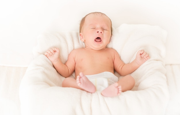 Portrait of cute baby boy lying in bed and yawning