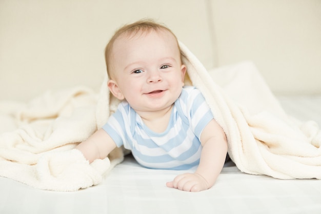 Portrait of cute baby boy lying under blanket