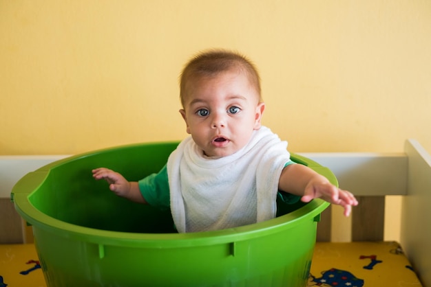 Photo portrait of cute baby boy sitting in bucket at home