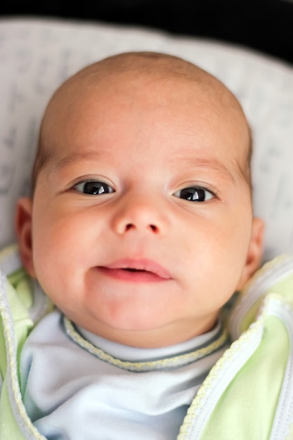 Portrait of cute baby close-up. Sweet little infant looks to camera. Bald baby with brown eyes and long lashes