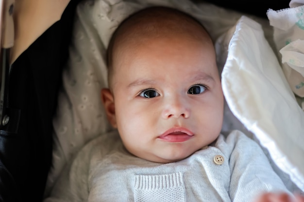 Portrait of cute baby close-up. Sweet little infant looks to camera. Bald baby with brown eyes and long lashes