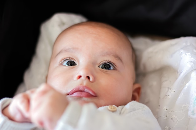 Portrait of cute baby close-up. Sweet little infant looks to camera. Bald baby with brown eyes and long lashes