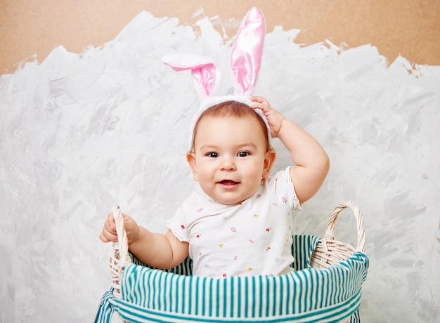 Portrait of a cute baby dressed in Easter bunny ears in a basket holds egg