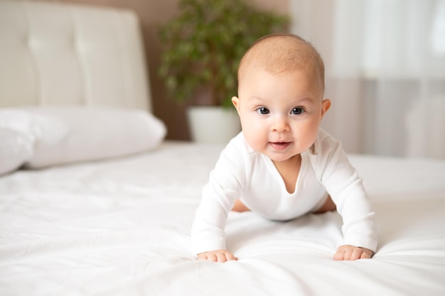 Portrait of a cute baby girl of 5 months in a white bodysuit on a white bed Space for text Child